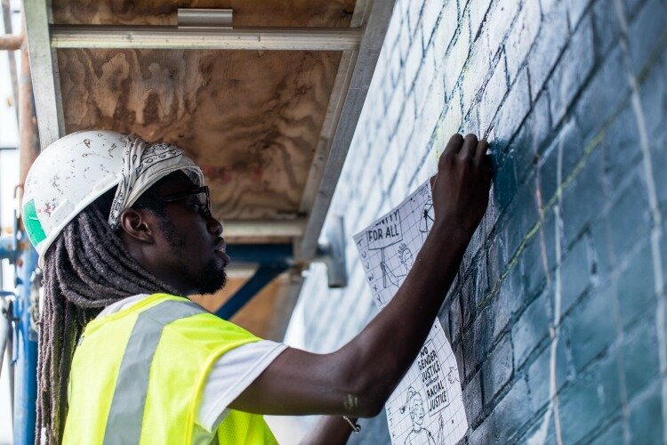 Prince Lang, ArtWorks junior teaching artist, transfers the initial YWCA’s 150th anniversary mural drawing to the wall. Lang worked with two other teaching artists and 12 youth apprentices. 